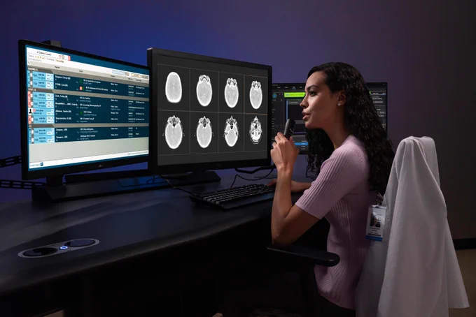 Radiologist seated at a workstation reviewing medical imaging scans and structured reporting data across multiple monitors in a clinical reading environment.