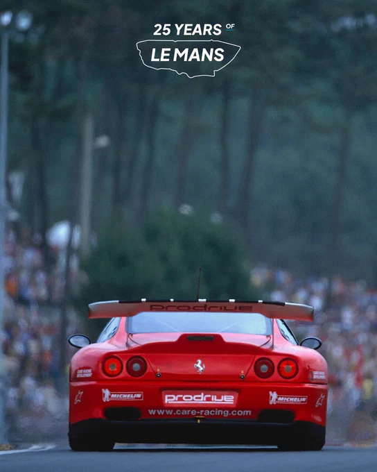 Rear view of the Prodrive Ferrari 550 GTS LM race car accelerating through a forest lined section of the Le Mans circuit, large rear wing visible, spectators packed along both sides.