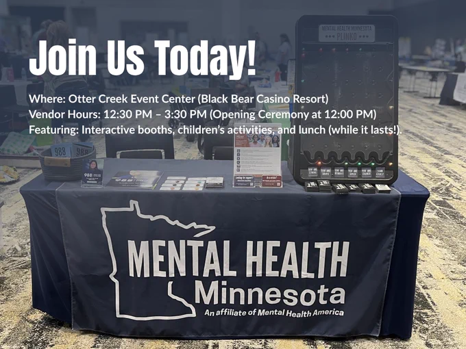 An exhibition table for Mental Health Minnesota at an indoor health fair, with a dark blue overlay at the top featuring white text.
The text reads: "Join Us Today! Where: Otter Creek Event Center (Black Bear Casino Resort). Vendor Hours: 12:30 PM – 3:30 PM (Opening Ceremony at 12:00 PM). Featuring: Interactive booths, children’s activities, and lunch (while it lasts!)."
Below the text, the original image is visible, showing the dark blue tablecloth with the "Mental Health Minnesota" logo and a white outline of the state. On the table are 988 Lifeline pamphlets, community resources, and a tabletop Plinko game with flashing lights.