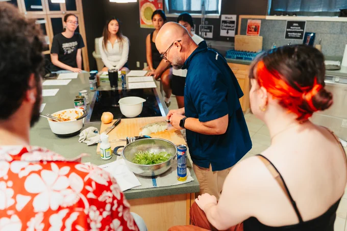 Person demonstrating how to prepare a dish while students look on.