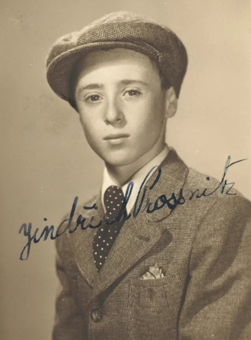 Portrait of a teenage boy wearing a tweed cap and jacket with a polka dot tie and a handkerchief in the breast pocket. The photograph is sepia-toned, and there is a cursive signature in the middle.