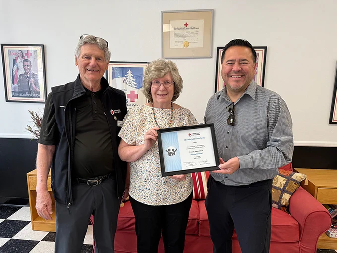 A woman stands with two men, holding a certificate of appreciation