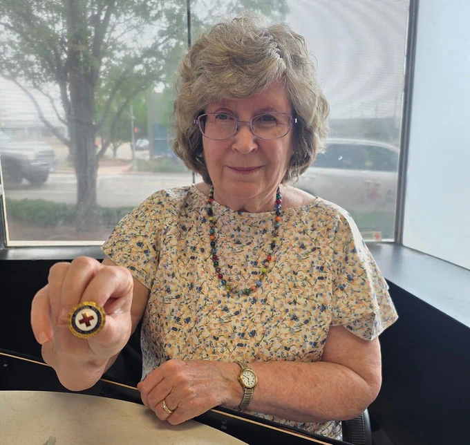 A woman holds out a Red Cross pin to the camera
