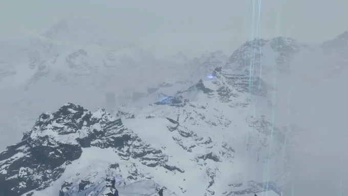 Verschneite und neblige Berge in Death Stranding Directors Cut. Schwarze Felsen ragen aus dem Schnee und feine blaue Lichtfäden des chiralen Netzwerks steigen in den trüben Himmel hinauf.