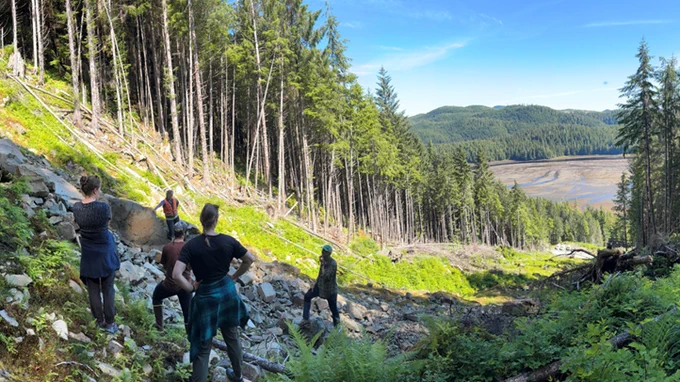 People standing on the side of a steep hill with trees in the background. 