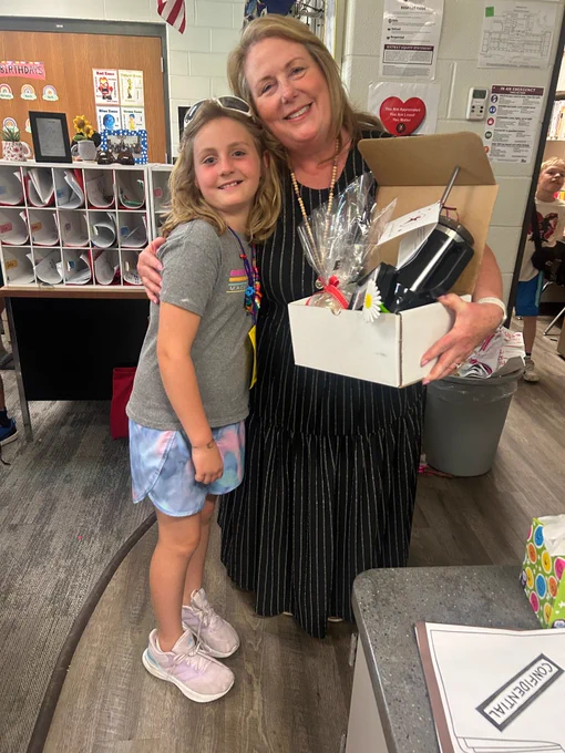 Teacher holds thank you gift and hugs student.