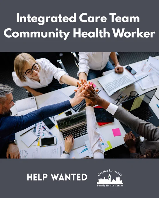 Diverse team joining hands over a cluttered desk with laptops and documents, symbolizing collaboration in community health work.