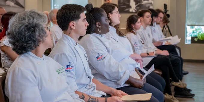 A group of graduates in white uniforms seated in a row, attentively listening during the HCTI graduation ceremony.