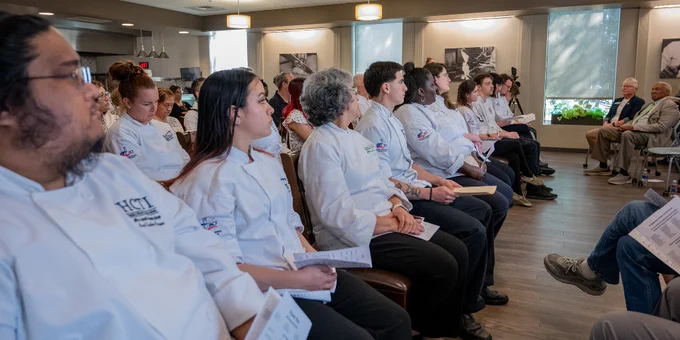 Group of culinary students in white chef jackets seated attentively during the HCTI graduation ceremony.