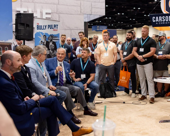 A panel of speakers engage with an audience at a convention, discussing a topic associated with 'The Bully Pulpit' podcast. The atmosphere is professional and engaged.