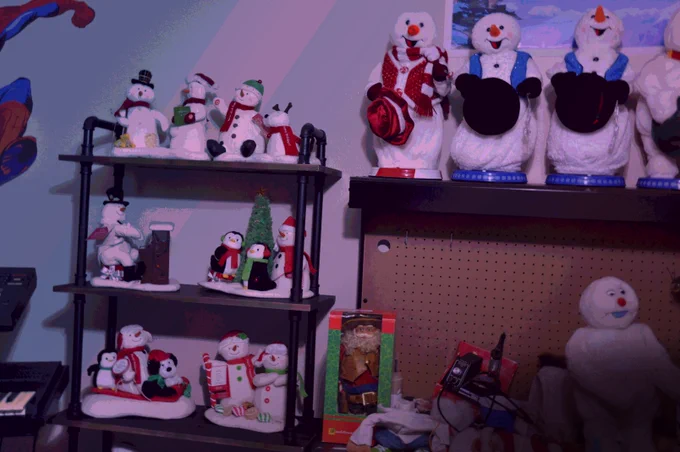 Various singing, dancing snowman decorations lined up on shelves. A work table sits next to them with various disassembled dancing Santas and snowmen. ✅
