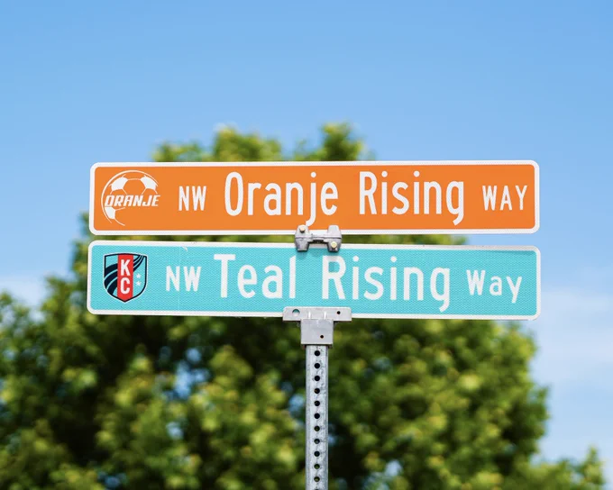 Close up of our street signs at the training center that has an “NW Oranje Rising Way” orange sign above our teal sign that says “NW Teal Rising Way”