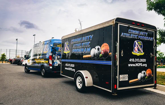 Howard County Police Department's Community Athletic Program van and trailer parked in a parking lot.