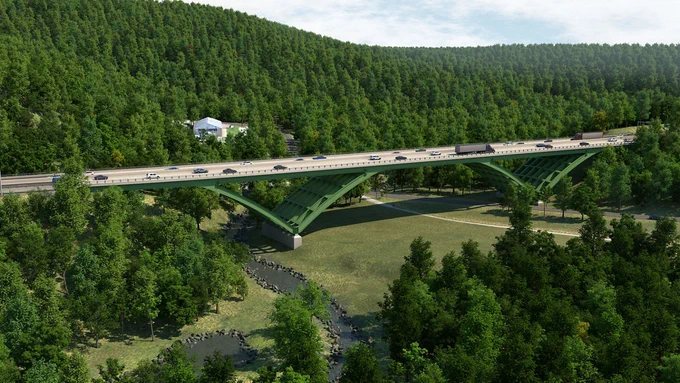A green bridge spans over a dense forested area with a small river below. The bridge carries vehicles traveling in both directions.