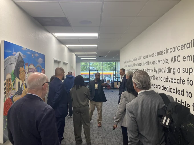 Group of professionals engaged in a discussion in a modern office hallway with large windows and wall text about ARC's mission.