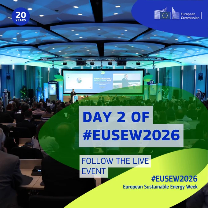 Promotional graphic for the European Sustainable Energy Week 2026 (EUSEW2026). A large conference hall filled with attendees facing a stage with presentation screens and speakers under a blue-lit ceiling. The European Commission logo appears in the top right, and a “20 Years” badge is shown in the top left. Overlaid text reads: “DAY 2 OF #EUSEW2026” and “FOLLOW THE LIVE EVENT.” Additional text at the bottom right reads: “#EUSEW2026 European Sustainable Energy Week.” Green and blue graphic shapes overlay the photo.