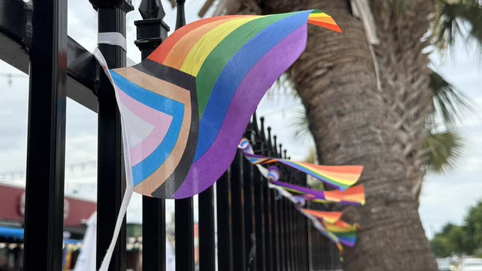 A row of pride flags hanging along a metal fence.