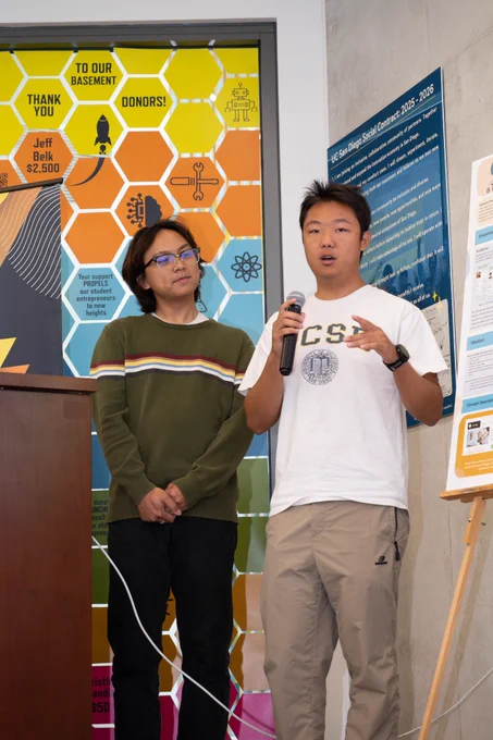 Two people speaking towards the camera, one person holding a microphone