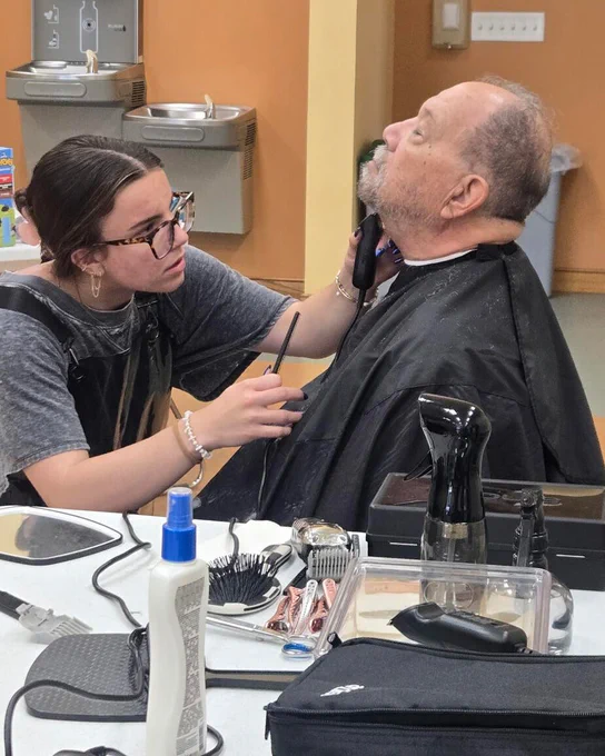 A cosmetology student trims a man’s beard during a free community haircut event.