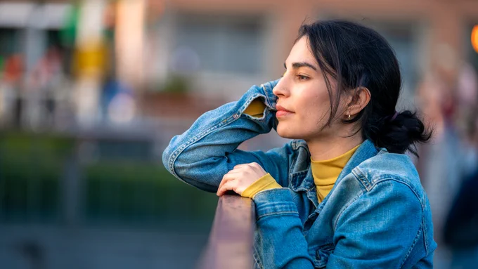 Woman in a denim jacket and yellow shirt leaning on a railing outdoors