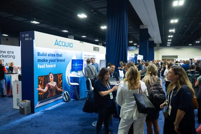 Crowded exhibition hall with attendees visiting the Acquia booth promoting brand-building websites.