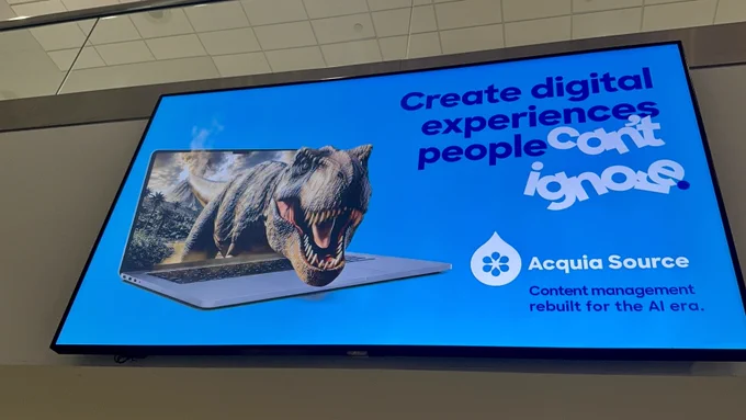 Digital billboard showing a roaring T-Rex emerging from a laptop screen with text promoting Acquia Source for AI-era content management.