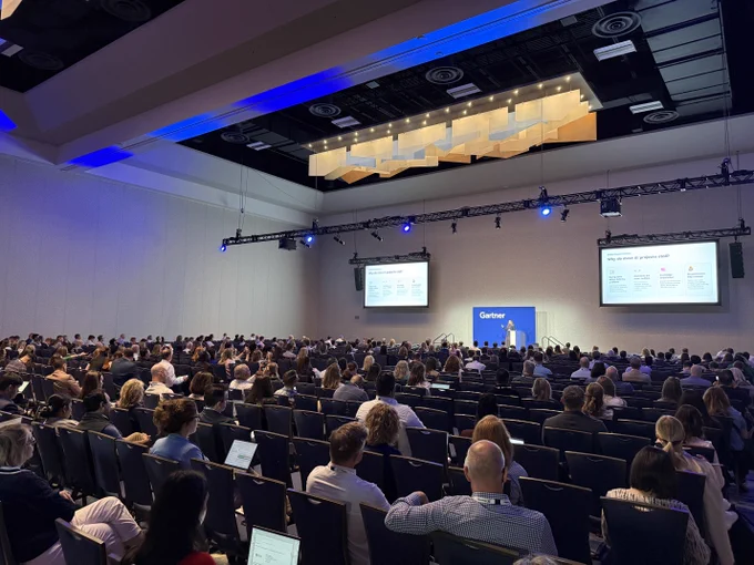 Large audience attentively listening to a speaker presenting slides at a Gartner conference in a spacious, modern auditorium.
