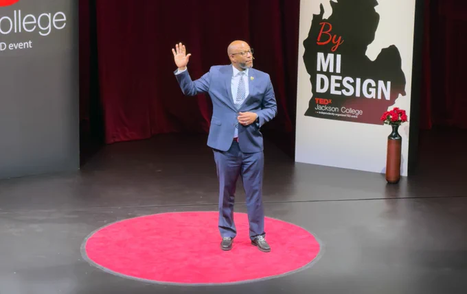 John Randle Sr. gestures while delivering a TEDx talk on a red circular carpet at Jackson College.