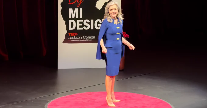 Chris Gorton stands on a red circular carpet delivering a TEDx talk at Jackson College.