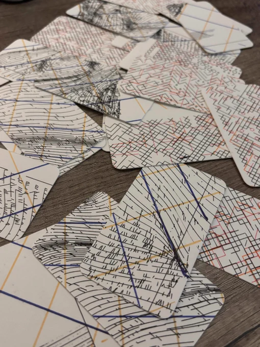 Scattered cards with geometric patterns of intersecting blue, red, and ochre lines on a dark wood surface.