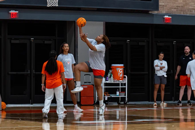 Player finishes a layup drill during the first day of summer practice as coaches and teammates look on.