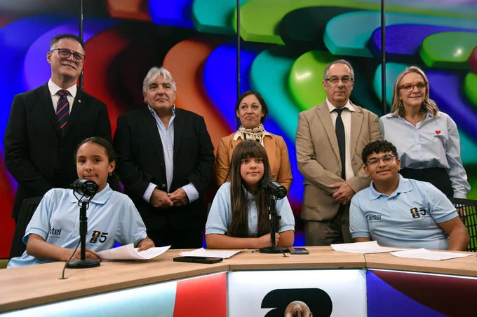 Adolescentes del abrojo, sentadas (dos) y sentado, con camisetas celestes; de pie, autoridades: director de Dinatel, Pablo Siris; presidente de Antel, Alejandro Paz; ministra Fernanda Cardona; ministro José Carlos Mahía; y presidenta del Secan, Erika Hoffmann (de izquierda a derecha). Detrás, pantalla de colores.