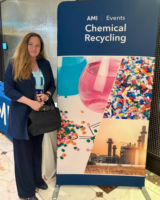 Stefanie Steenhuis poses beside an AMI Events popup display, showing the AMI logo and several photos depicting plastic recycling, chemistry, and refinement.