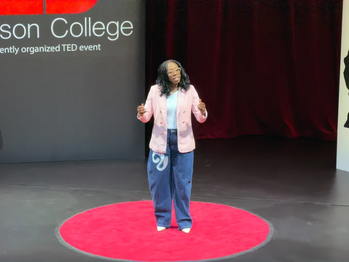Speaker Jasmine Isaac Ofori delivering a TEDx talk on a red circular stage at a college event.