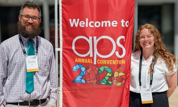 A man and woman flanking a red banner that reads in white, gold, and patterned text, "Welcome to aps ANNUAL CONVENTION 2026"