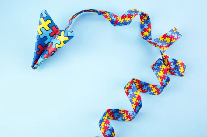Fita colorida com estampa de quebra-cabeça forma espiral e avião de papel sobre fundo azul-claro. Imagem: nambitomo/Getty Images/Canva.