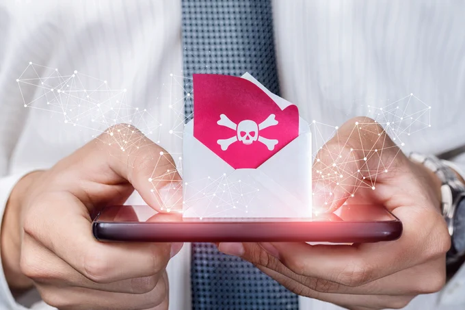 Person in business attire holding a smartphone displaying a red warning icon with a skull and crossbones symbolizing a threat.