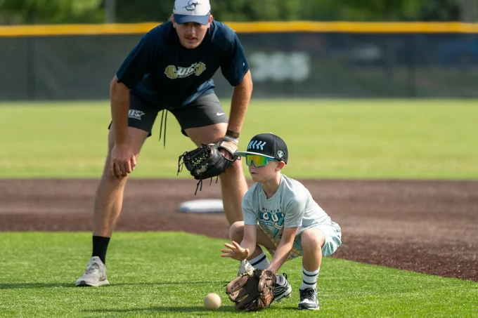 Youth baseball camper fields a ground ball while a UIS player demonstrates proper technique on the infield.