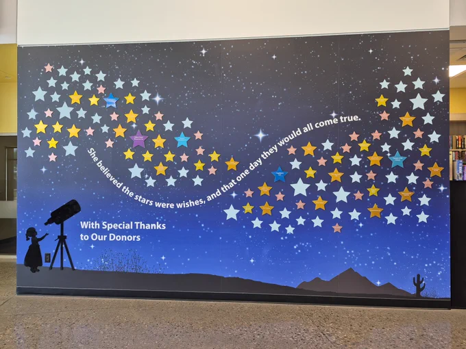 A mural of a night sky filled with colorful stars forming a swirling pattern and a quote about wishes coming true, with a silhouette of a child looking through a telescope.