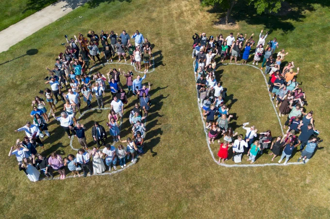 drone photo of around a hundred people standing together to form a large '60.'