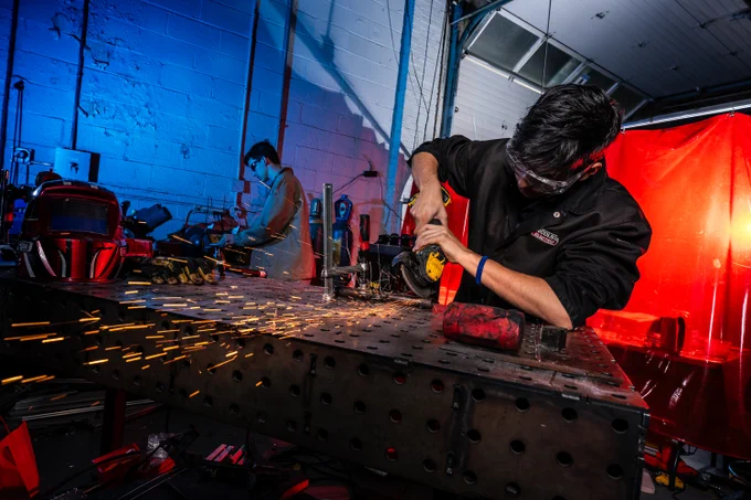 A person using a saw in a workshop environment, with blue lighting on the left and red lighting on the right