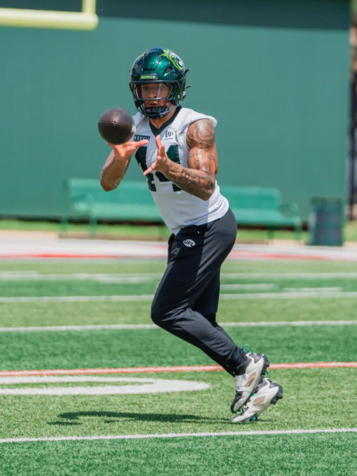 A football player in a practice uniform and helmet prepares to catch a ball on a grassy field. The setting is dynamic and focused.