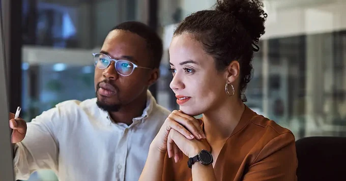 Two colleagues engaged in a focused discussion in a modern office, one gesturing while the other listens attentively.
