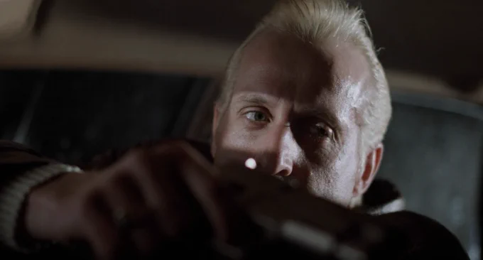 another closeup of Stormare, only his eyes illuminated, bottom half of his face obscured by his right hand and the gun he's holding in it 