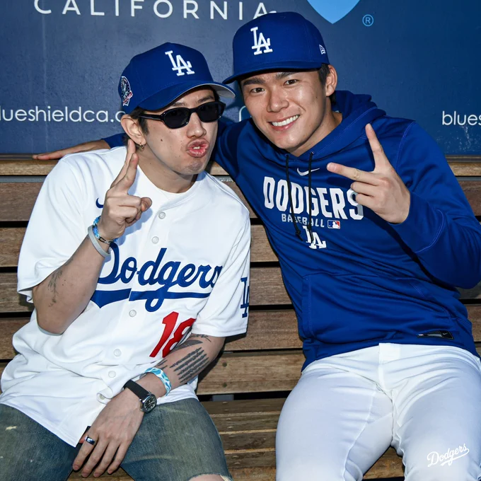 A photo of Yoshinobu Yamamoto and Taka from ONE OK ROCK posing for a photo while sitting in the dugout.
