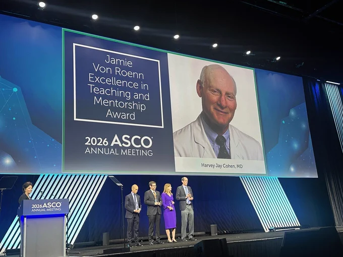 Stage at the 2026 ASCO Annual Meeting featuring a large screen displaying the 'Jamie Von Roenn Excellence in Teaching and Mentorship Award' and an image labeled 'Harvey Jay Cohen, MD.' Four individuals stand below the screen, three holding plaques.