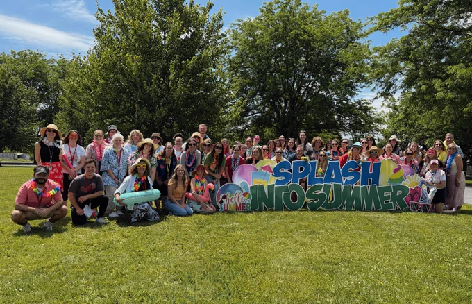 Group of people posing for photo outdoors with "Splash into Summer" sign on grass