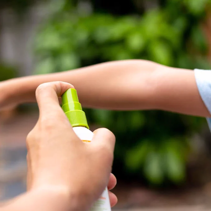 Someone sprays bug repellent on their bare arm.