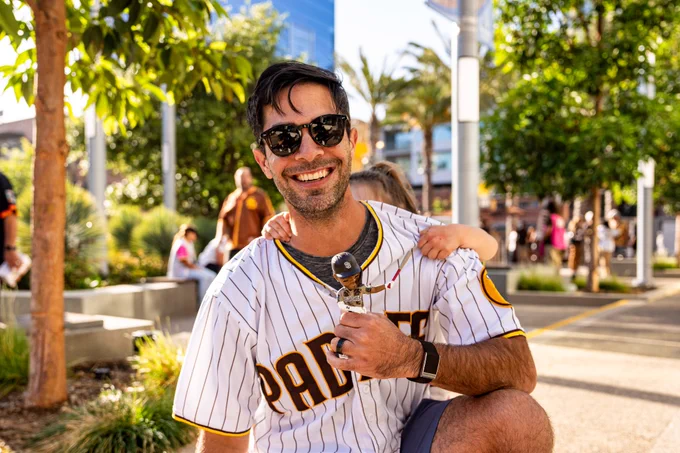 Photo of a Padres fan holding their "Bogey Goes Boom" bobblehead giveaway. They are smiling for the camera. They are wearing the Padres home white pinstripe jersey.