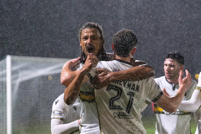 A passionate soccer team celebrates a goal in the rain. The players are visibly excited, showcasing teamwork and enthusiasm.